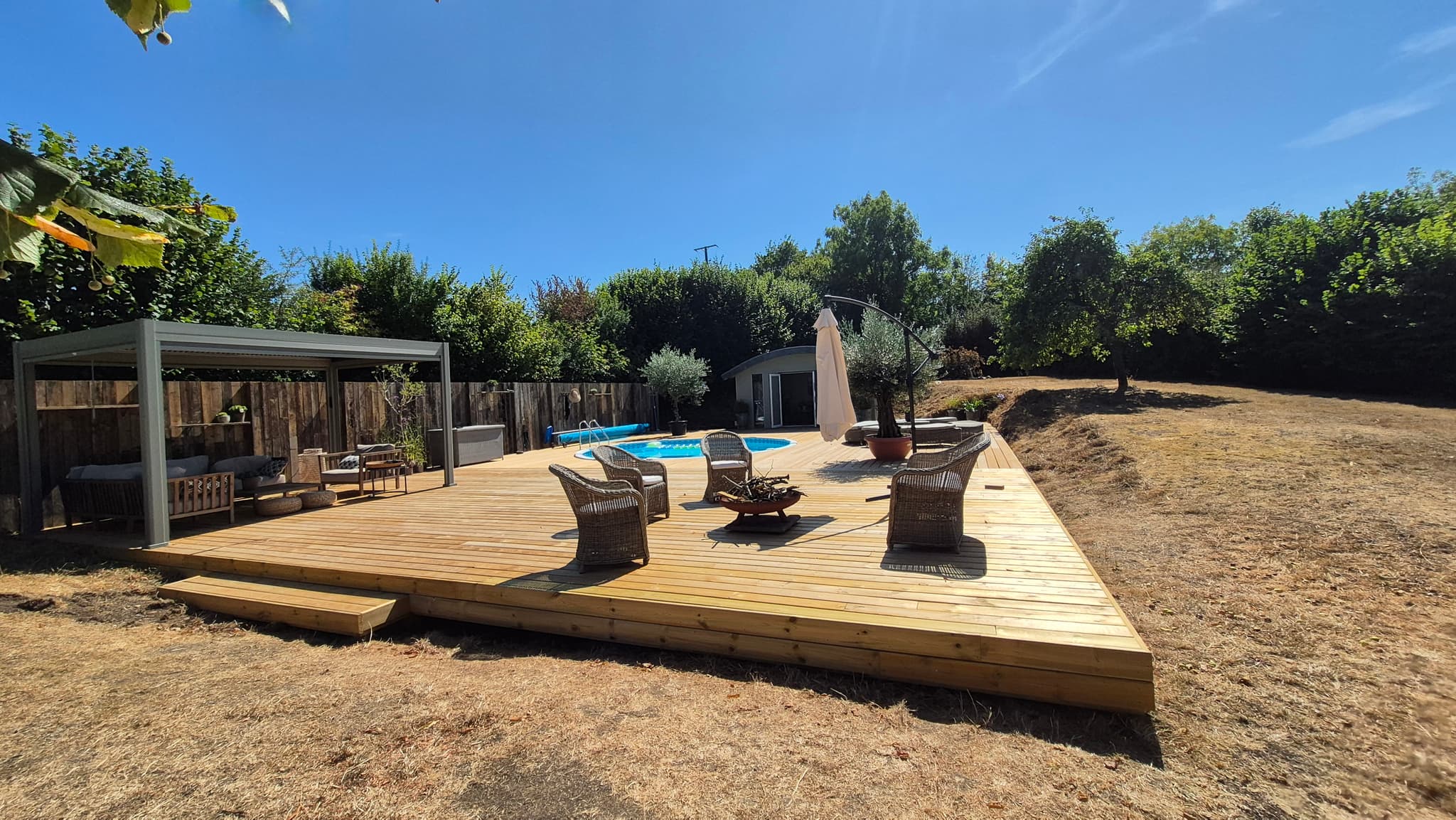 The finished deck with seating around a fire bowl, pool and pergola beyond