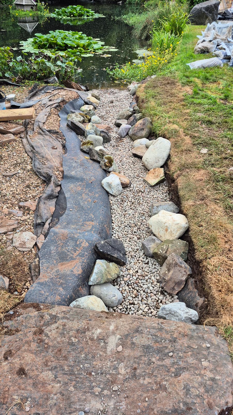 Stone edging and a fresh pebble bed being set into the new channel